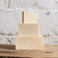 Three stacked soap bars on a wooden surface with a textured white background