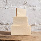 Three stacked soap bars on a wooden surface with a textured white background
