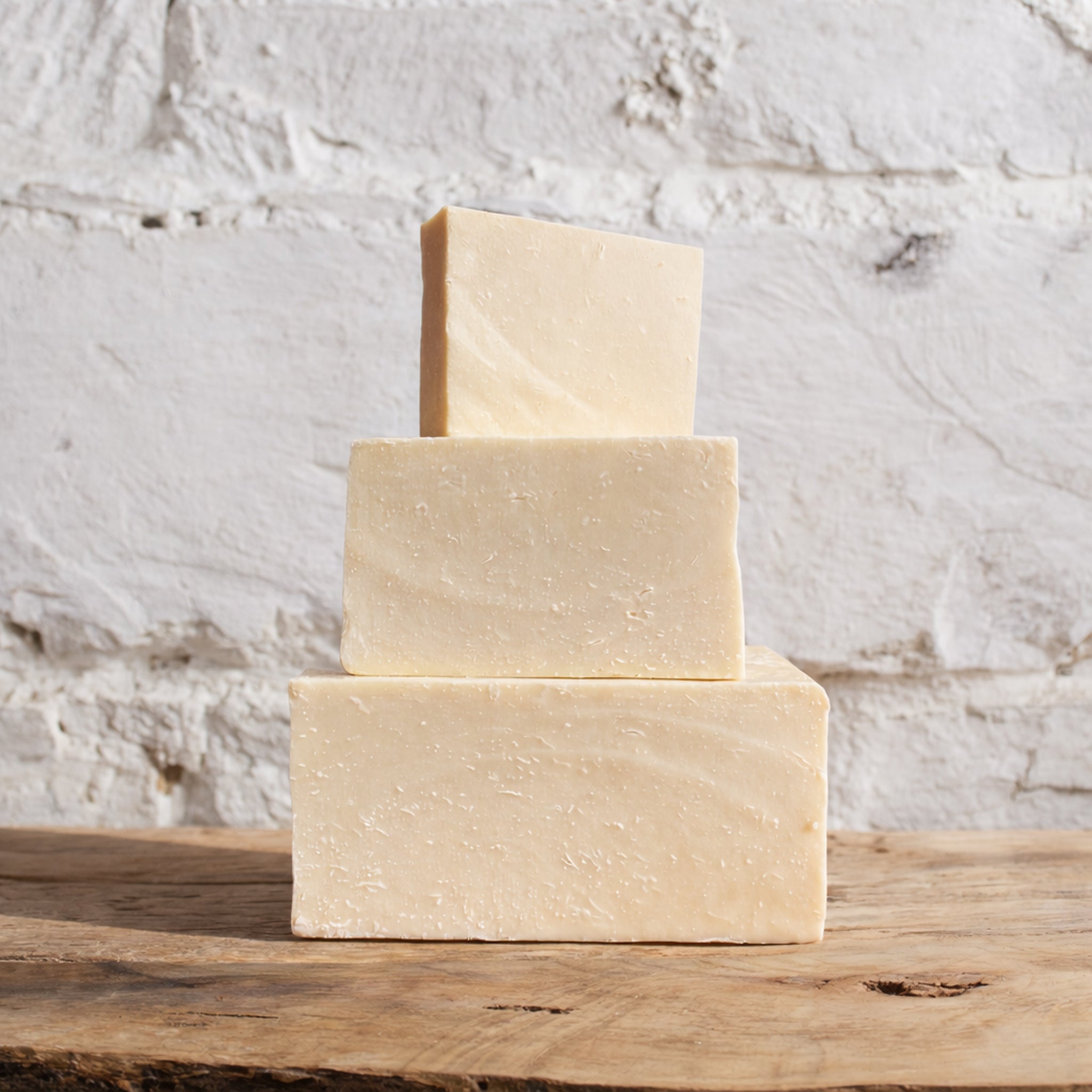 Three stacked soap bars on a wooden surface with a textured white background