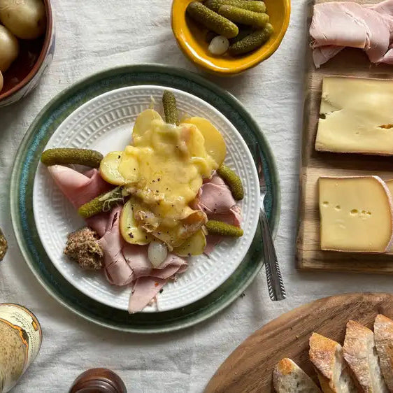 Plated dish with potatoes, ham, and pickles on a table with various condiments and bread.