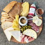 Wooden platter with assorted cheeses, meats, and bread on a concrete surface