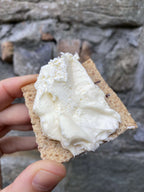 Cracker with cream cheese held in front of a stone wall