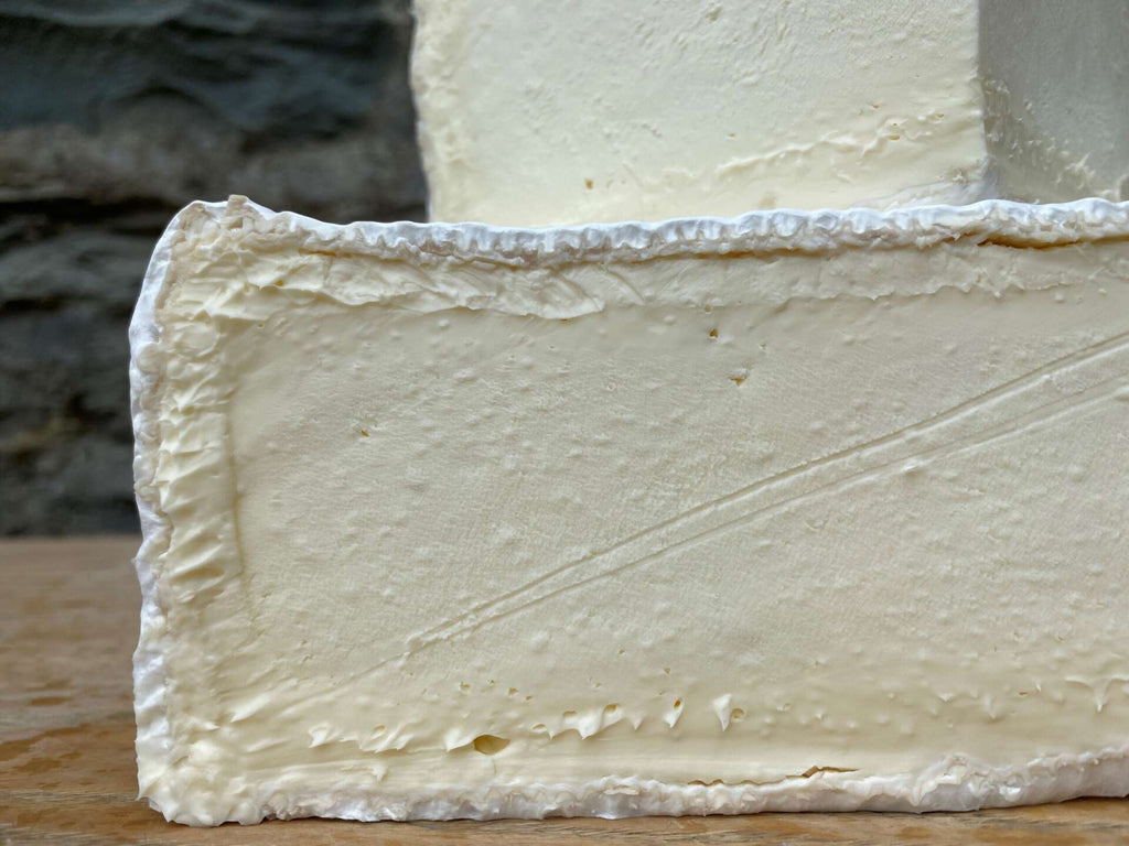 Close-up of a block of cheese with a soft, porous texture on a wooden surface.