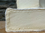 Close-up of a block of cheese with a soft, porous texture on a wooden surface.