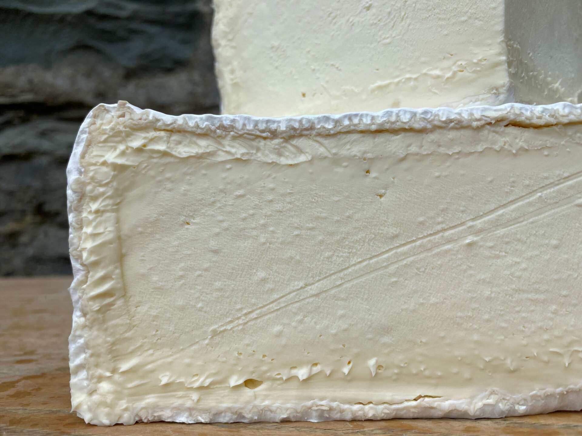Close-up of a block of cheese with a soft, porous texture on a wooden surface.