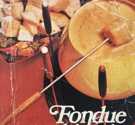Two forks dipping into a cheese fondue pot on a red surface