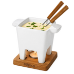 White fondue pot with wooden handles on a wooden base, filled with cheese fondue and garnished with herbs.