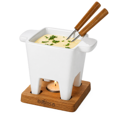 White fondue pot with wooden handles on a wooden base, filled with cheese fondue and garnished with herbs.