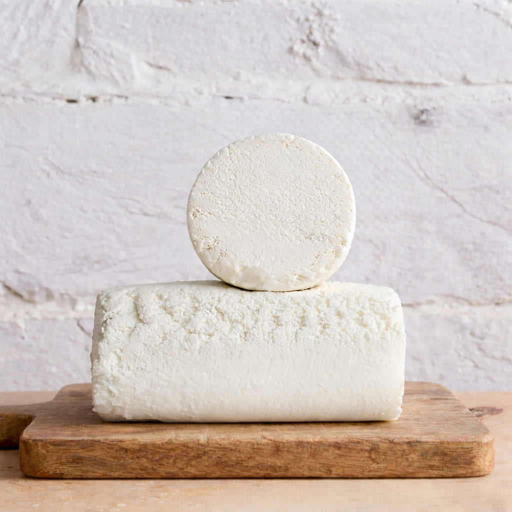 Two blocks of white cheese stacked on a wooden board with a light gray background