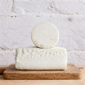 Two blocks of white cheese stacked on a wooden board with a light gray background
