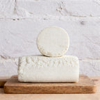 Two blocks of white cheese stacked on a wooden board with a light gray background