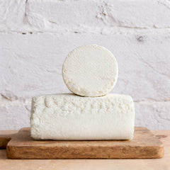 Two blocks of white cheese stacked on a wooden board with a light gray background