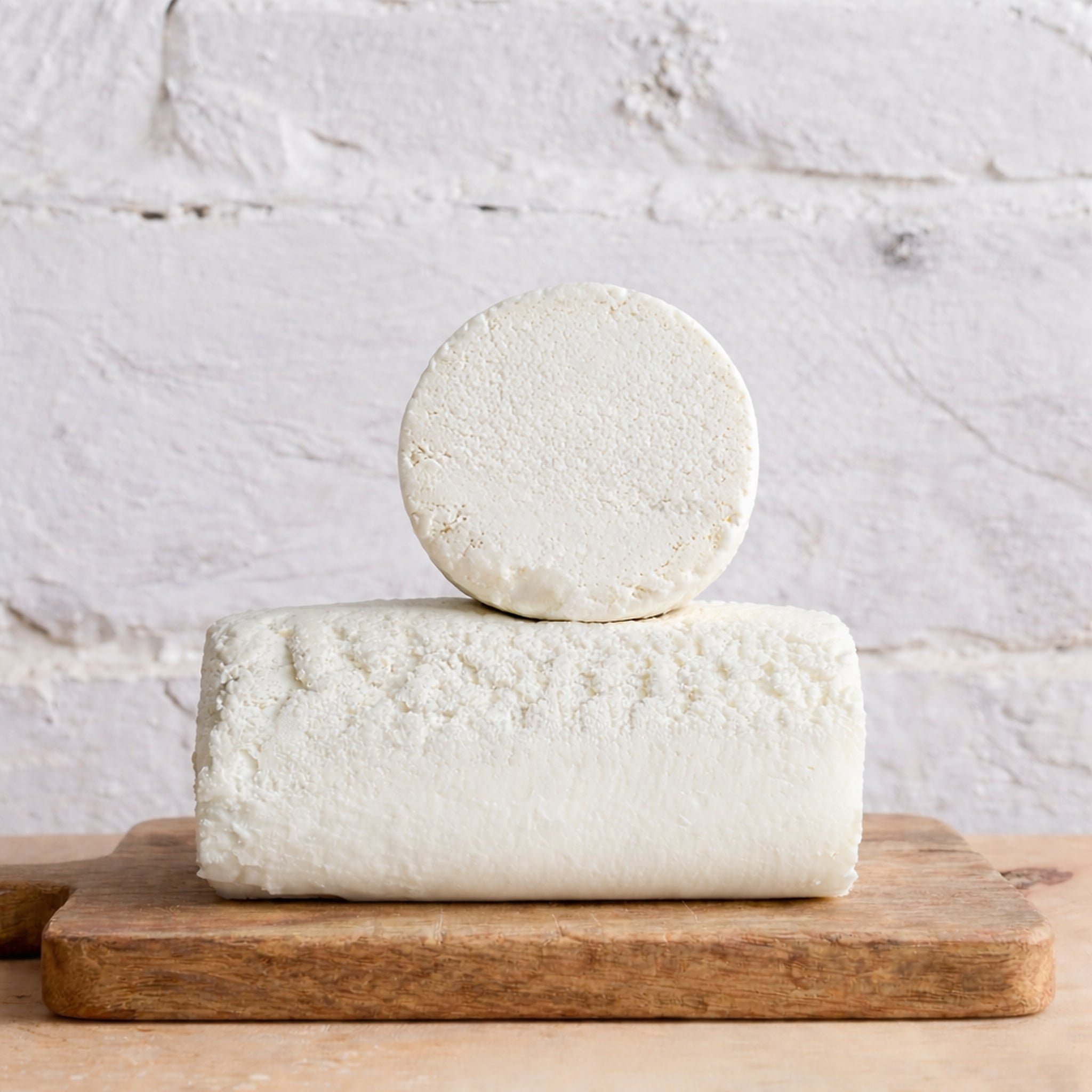 Two blocks of white cheese stacked on a wooden board with a light gray background