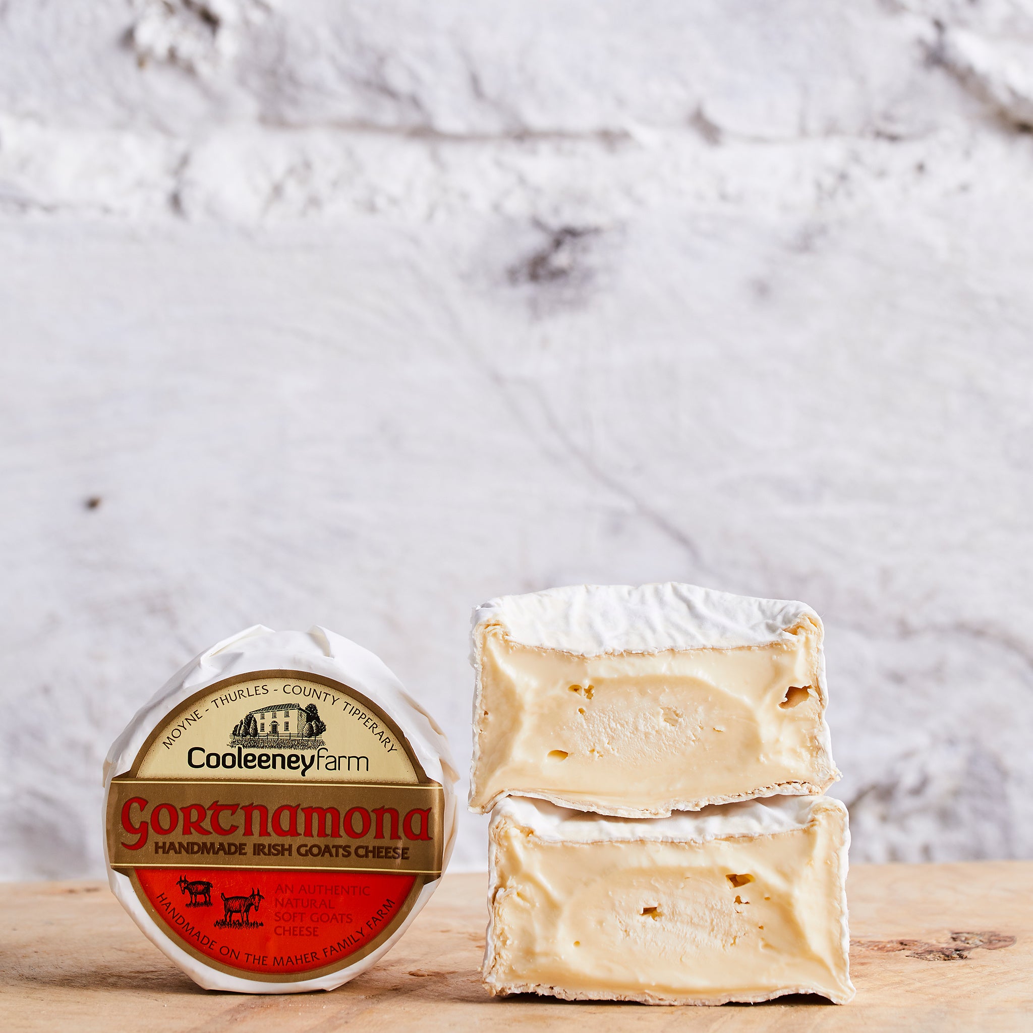 Two blocks of Gortnamona goat's cheese with its packaging on a wooden surface.