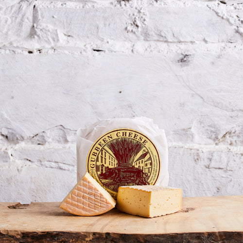 Two pieces of cheese on a wooden board with a Gubbeen Cheese branded paper in the background.