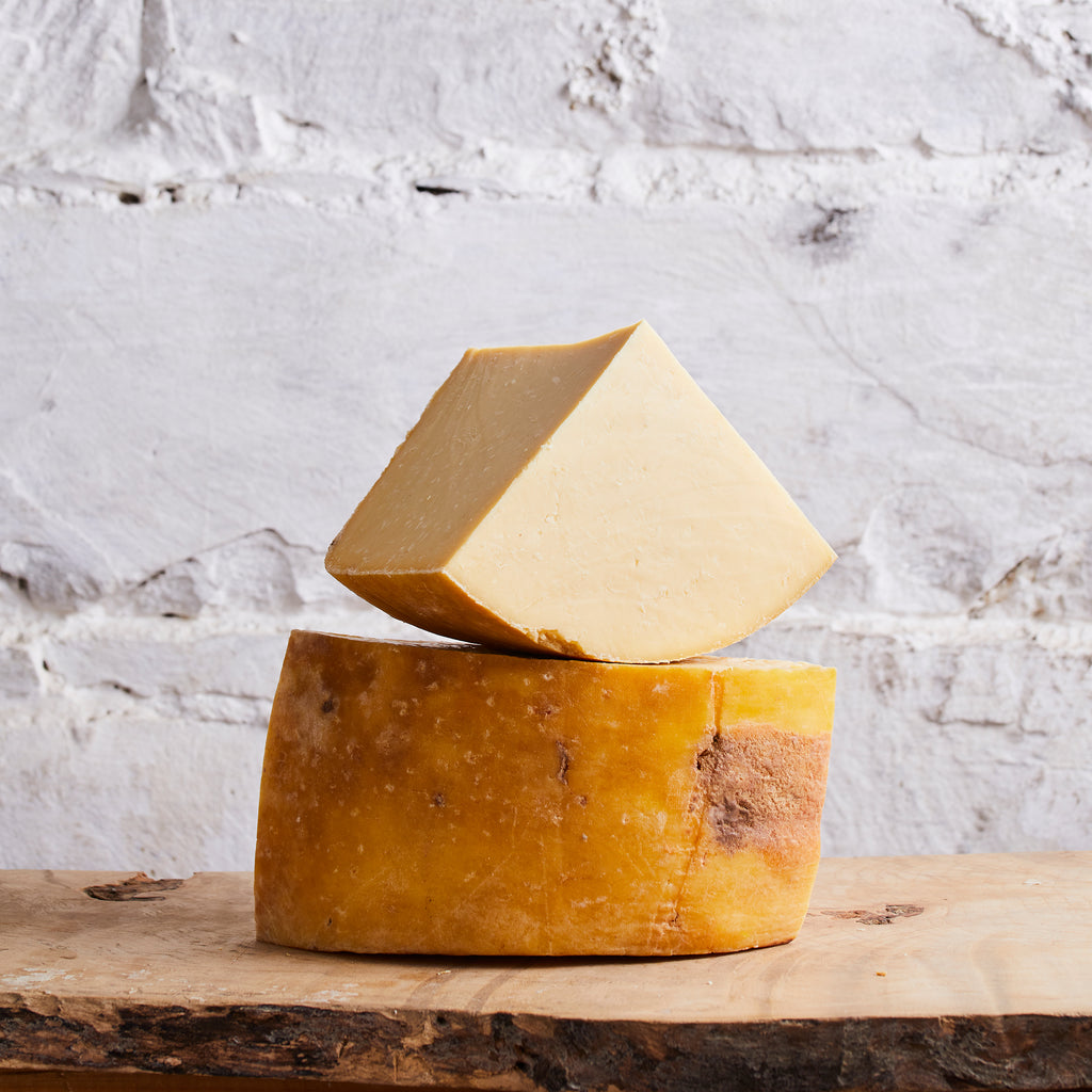 Two pieces of cheese, one stacked on top of the other, on a wooden surface with a textured white background.