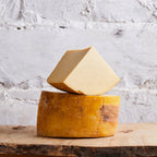 Two pieces of cheese, one stacked on top of the other, on a wooden surface with a textured white background.
