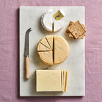 Assorted cheeses on a marble board with a knife on a pink textured background