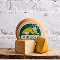 Wheel and wedges of Killeen cumin studded goats cheese against a white brick wall