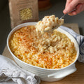 Spoon lifting macaroni cheese from a white baking dish