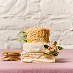 Three types of cheese stacked with crackers and flowers on a textured surface