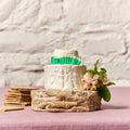 Decorative cheese wheel with crackers and flowers on a pink surface