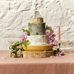 Tiered cheese celebration cake decorated with pink flowers on a terracotta cloth