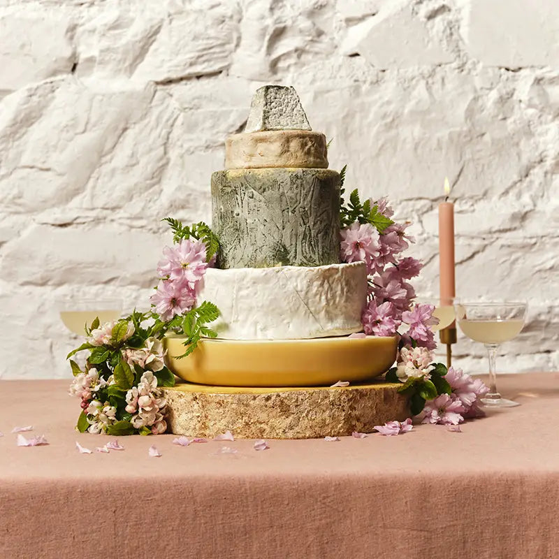 Tiered cheese celebration cake decorated with pink flowers on a terracotta cloth