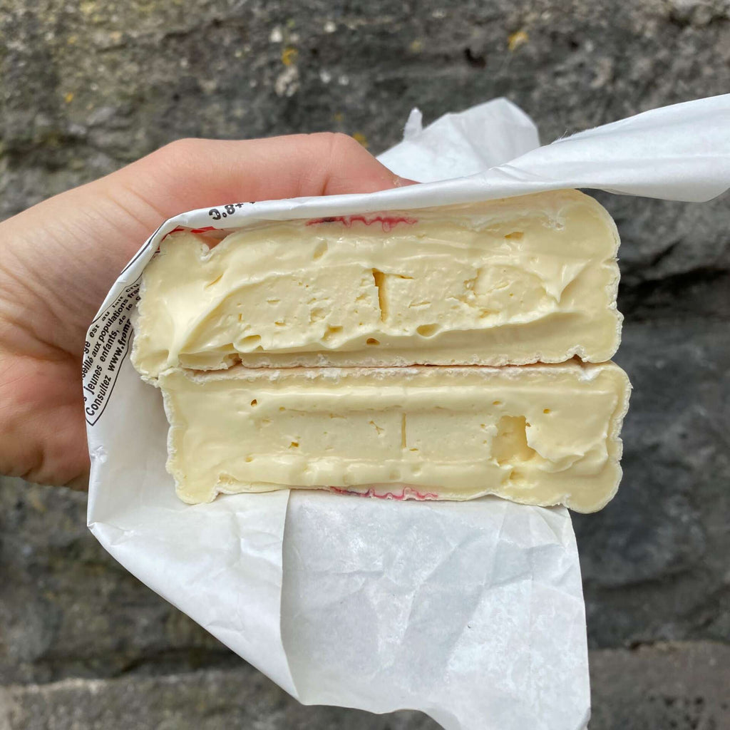 Hand holding a block of cheese wrapped in paper against a stone wall background