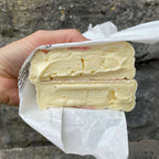 Hand holding a block of cheese wrapped in paper against a stone wall background