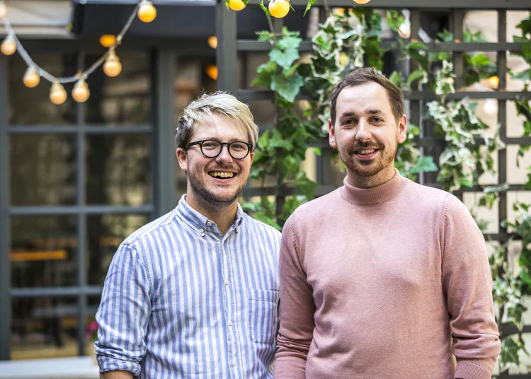 Russell Alford and Patrick Hanlon standing together in front of a plant covered wall