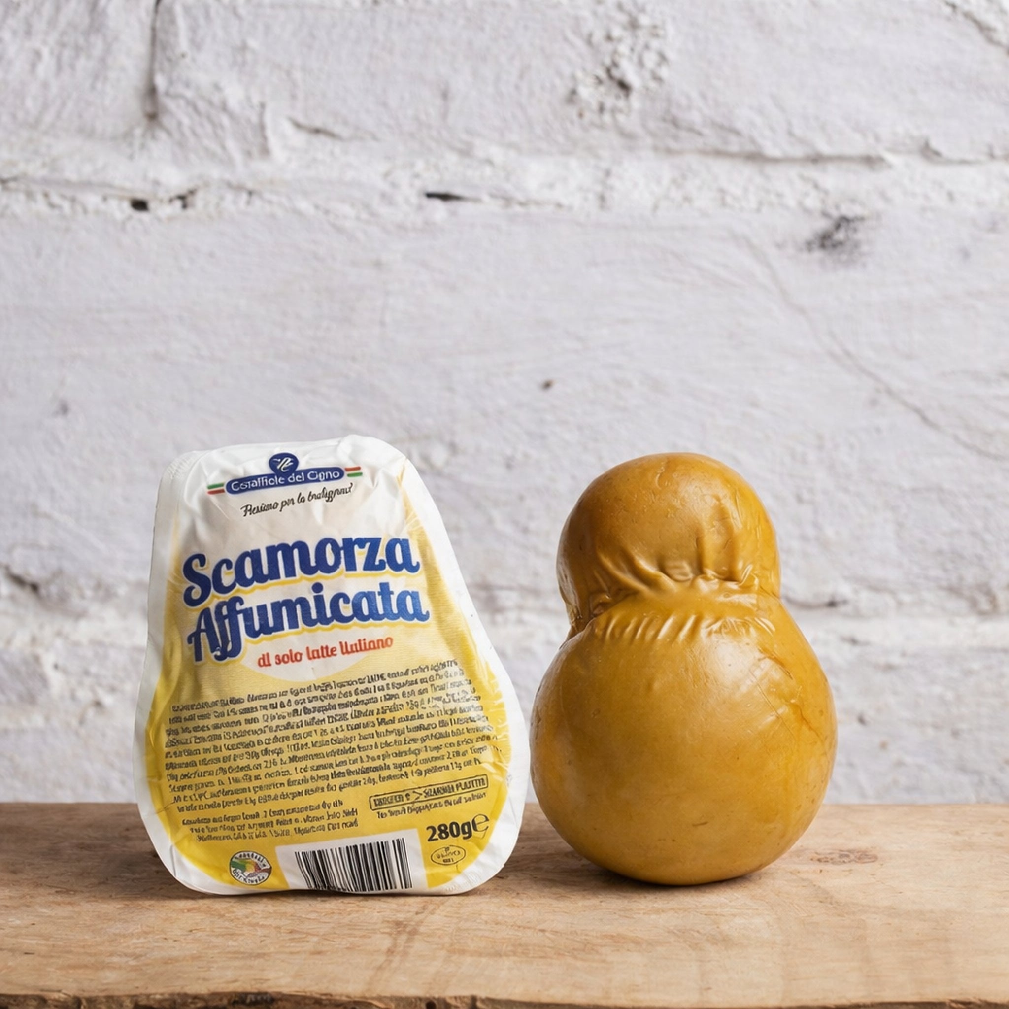 Packaged Scamorza Affumicata cheese on a wooden surface with a white brick wall background