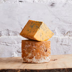 Two blocks of cheese stacked on a wooden surface with a textured white background