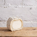 Half-cut wheel of cheese on a wooden board with a white textured background