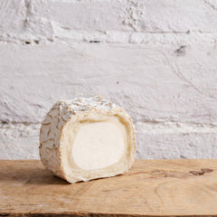 Half-cut wheel of cheese on a wooden board with a white textured background
