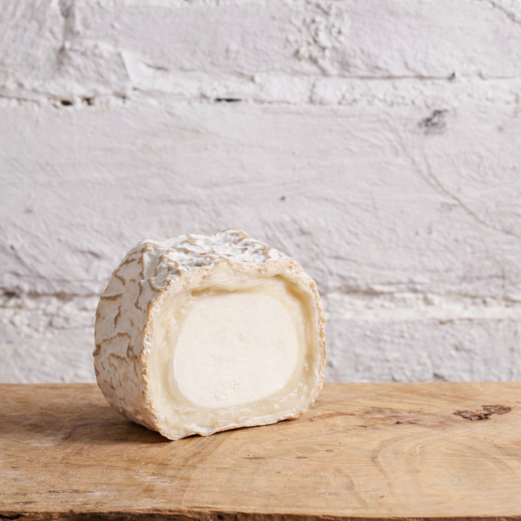 Half-cut wheel of cheese on a wooden board with a white textured background