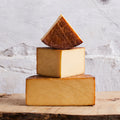 Three blocks of cheese stacked on a wooden surface with a marble background