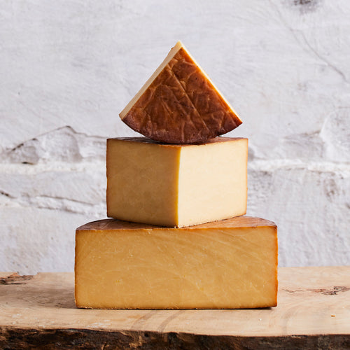Three blocks of cheese stacked on a wooden surface with a marble background