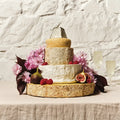 Tiered cheese celebration cake decorated with pink flowers and figs