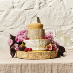 Tiered cheese celebration cake decorated with pink flowers and figs