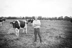 Black and white photograph of a farmer standing in a field with dairy cows