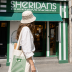 Person walking past Sheridans Cheesemongers store with a branded tote bag.