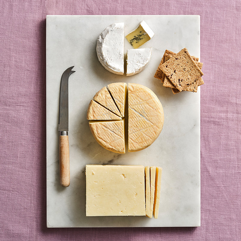 Assorted cheeses on a marble board with a knife on a pink textured background