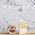 Wheel and wedge of Wicklow Bán cheese on a wooden board against a white wall
