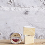 Wheel and wedge of Wicklow Bán cheese on a wooden board against a white wall